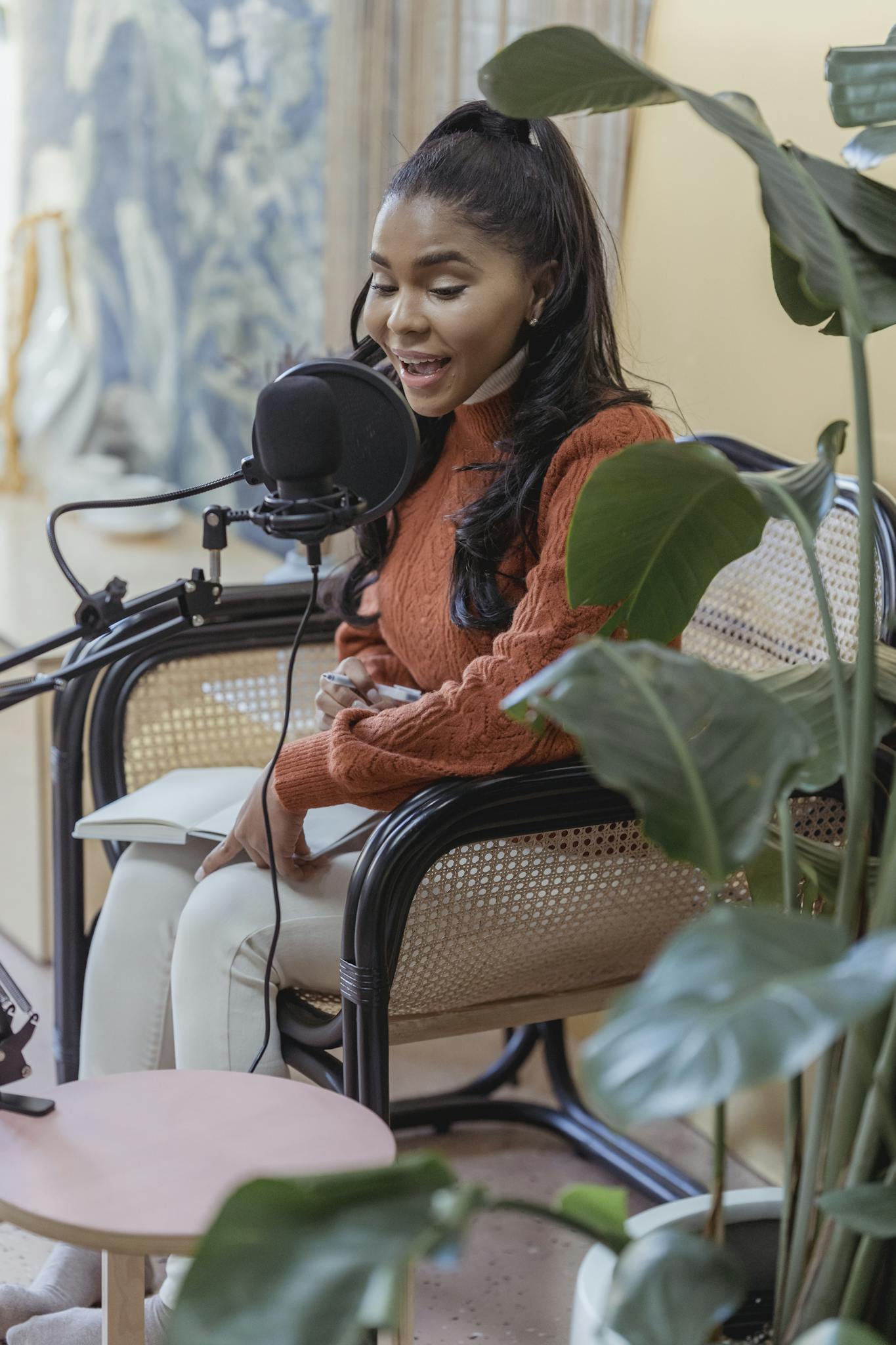 African American woman recording a podcast in an indoor studio with lush green plants.